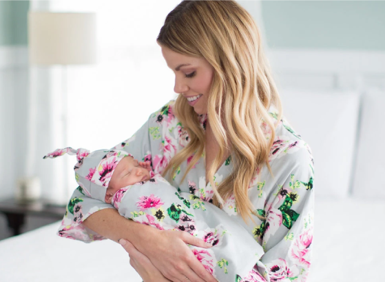 A mother holding her baby both are wearing a matching floral robe and a floral swaddle