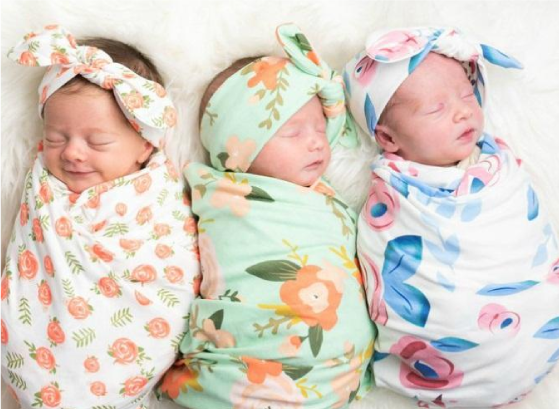 Three beautiful baby girls wearing a floral swaddle with a matching floral headband